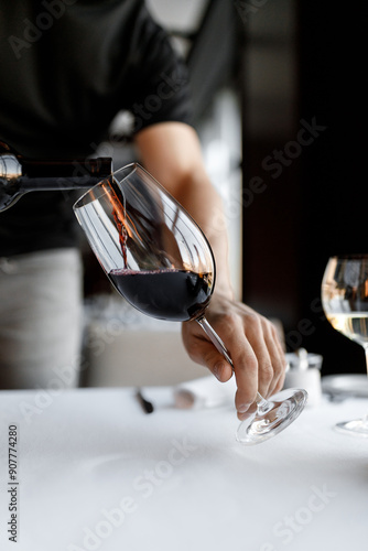 handsome bartender skillfully pours red wine into a glass on a beautiful white tablecloth in a nice restaurant
