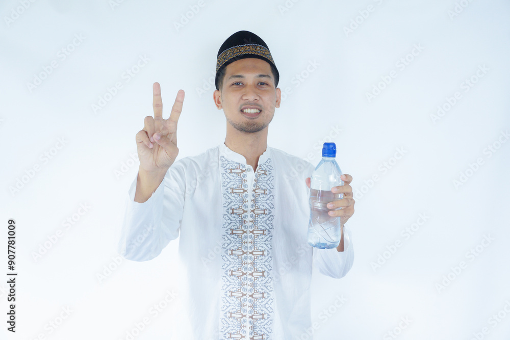 Moslem Asian man smiling and showing two fingers while holding a drinking water bottle Moslem Asian man smiling and showing two fingers while holding a drinking water bottle