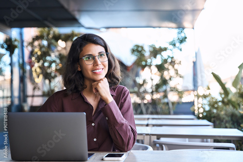Free Download Thoughtful young latin freelance girl student in eyeglasses using laptop pc sitting outdoors. Dreaming middle eastern indian business woman working on compute, looking pondering aside. Copy space - GFXLoad