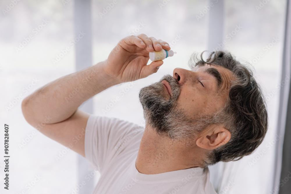 Close-up photo of an older gray-faced man who drips eye drops with medicine for pain and fatigue, sitting on the couch at home. Close-up photo of an older gray-faced man who drips eye drops with medicine for pain and fatigue, sitting on the couch at home.