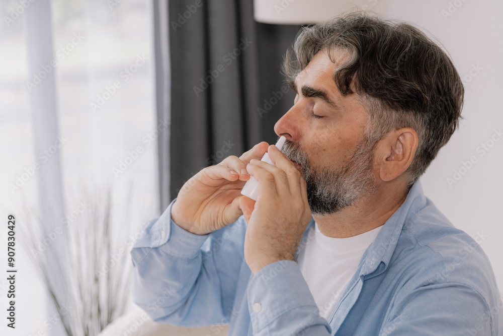 Elderly mature sick man in blanket suffering flu and cold using nasal spray at home. Rhinitis, medicine and healthcare concept Elderly mature sick man in blanket suffering flu and cold using nasal spray at home. Rhinitis, medicine and healthcare concept