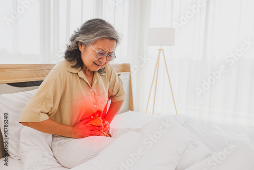 Obraz na plátně Elderly Asian woman had stomach pain with pained expression on her face while sleeping on the bed, holding her stomach with her hands in excruciating pain for no apparent reason
