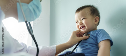 Smiling Asian baby boy receiving medical checkup from doctor with stethoscope, happy child in blue shirt at pediatric examination, healthcare concept.