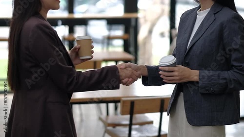 Two business professionals shaking hands while holding coffee cups in a modern office environment.