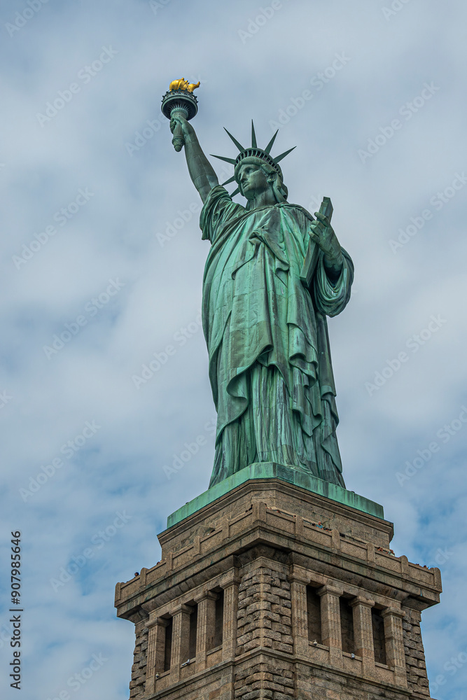 Fototapeta premium New York, NY, USA - August 4, 2023: Miss Liberty statue from under right, against blue cloudscape