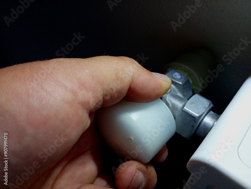 A person tightens the valve on the pipe of the heating system of the house. The topic of saving heat in winter.
