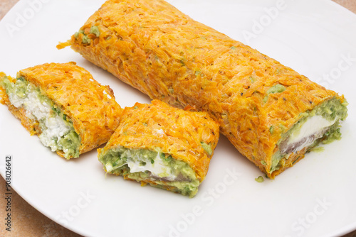 Close-up of a baked carrot roll with guacamole, with two cut pieces: one with a middle layer of creamy ricotta cheese and the other with cream cheese and marinated smoked salmon. Healthy food.