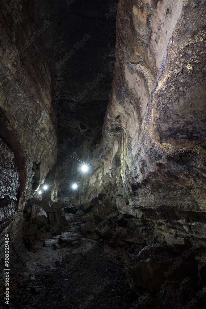 Dimly lit rocky cave passage with uneven rough walls and scattered stones Dimly lit rocky cave passage with uneven rough walls and scattered stones