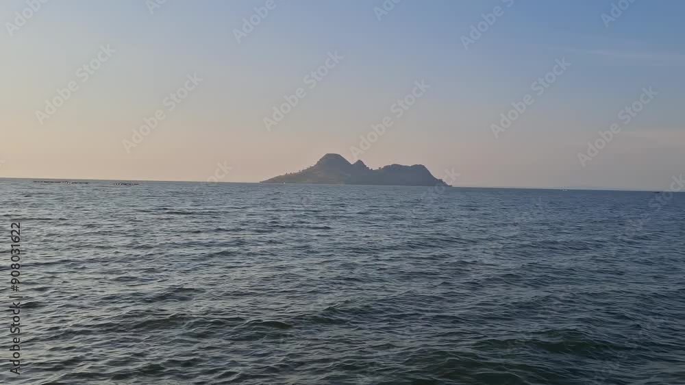 A lone island, bathed in the warm glow of the setting sun, rises majestically from the tranquil ocean waters. The image evokes a sense of serenity, mystery, and the allure A lone island, bathed in the warm glow of the setting sun, rises majestically from the tranquil ocean waters. The image evokes a sense of serenity, mystery, and the allure