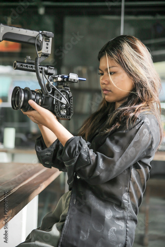 young Asian camera woman holding and filming with a professional video camera at vintage coffee shop