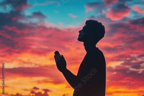 Prayer concept. Silhouette of a young man in a praying pose. Set against a vibrant sunset sunrise sky. Clasped hands. Also related to gospel, testimony, deliverance, providence, mercy, ai