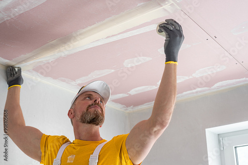 The worker make a plasterboard ceiling. He does taping plaster drywall ceiling joints. He is  putting fiberglass tape into the plaster putty. photo