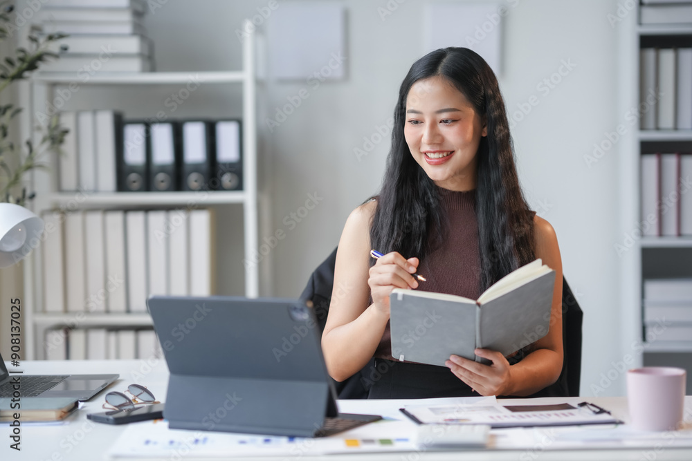 Young businesswoman is taking notes in her notebook while having a work video call on her tablet Young businesswoman is taking notes in her notebook while having a work video call on her tablet