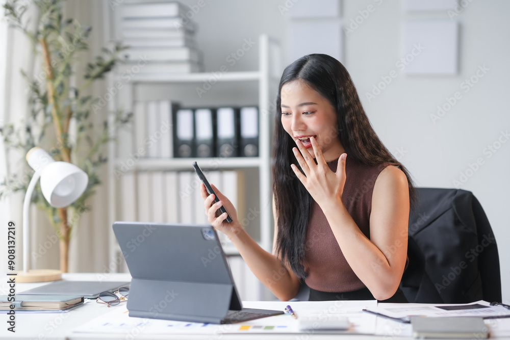 Excited asian businesswoman is using smartphone and laptop computer while working on desk in office Excited asian businesswoman is using smartphone and laptop computer while working on desk in office