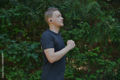 A man jogging using headphones in a park. A young man running outdoors on a summer day. The concept of fleetness, training and healthy lifestyle photo