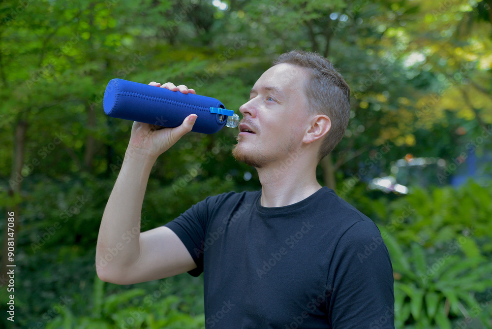 A man drinks water from a sports bottle after jogging in the park. Tired exhausted and thirsty after workout and running. The concept of fleetness, training and healthy lifestyle A man drinks water from a sports bottle after jogging in the park. Tired exhausted and thirsty after workout and running. The concept of fleetness, training and healthy lifestyle