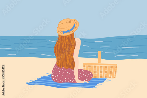 A woman sits on a beach, gazing at the ocean. She wears a sunhat and polka dot dress, with a picnic basket beside her on a blue blanket. Peaceful scene