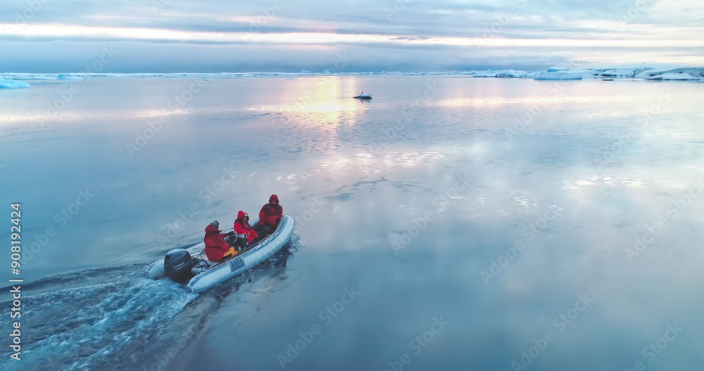 Fototapeta premium Group of scientists ride motorboat in Antarctica. Zodiac boat glides on ocean surface in sunset light. Antarctic travel and expedition. Discover beauty of South Pole. Aerial drone winter landscape