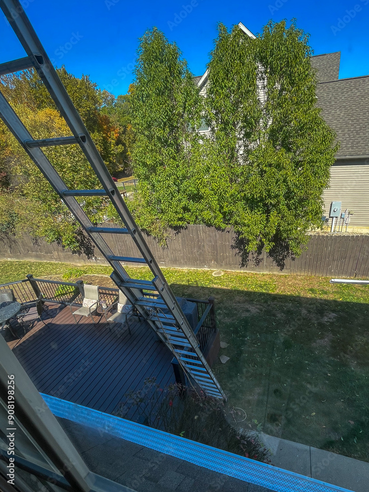 View out a window of a very tall, two story aluminum extension ladder on a house View out a window of a very tall, two story aluminum extension ladder on a house