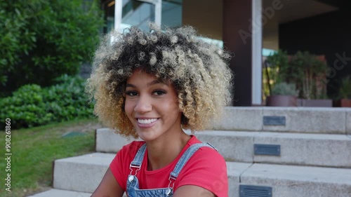 Portrait of young African American woman in denim overalls smiling at camera sitting outdoor photo