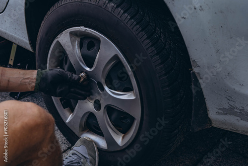 Young man in unscrewing lug nuts on car wheel in process of new tire replacement,using wrench while changing flat tire on the road.