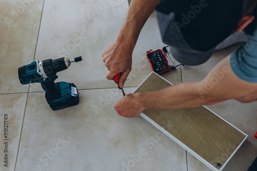  Close-up of a man's hands screwing screws into a wooden shelf on the floor using a screwdriver