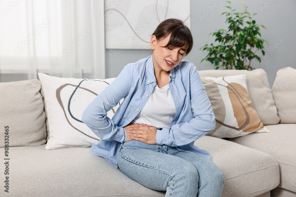 Upset woman suffering from abdominal pain on sofa at home Upset woman suffering from abdominal pain on sofa at home