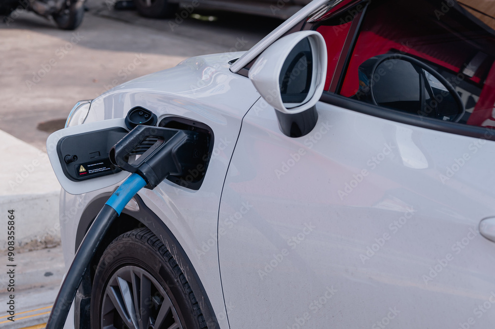 Sustainability concepts. Electric vehicles. A white car is being charged at a charging station. The car is parked in a parking lot Sustainability concepts. Electric vehicles. A white car is being charged at a charging station. The car is parked in a parking lot
