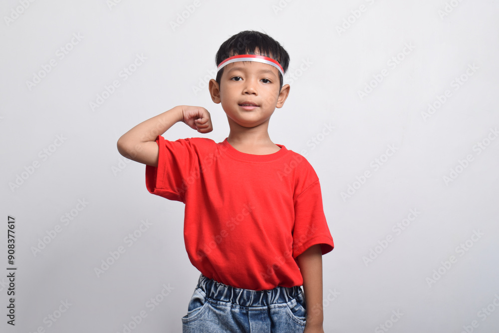 Confident Asian boy in red t-shirt flexing strength by raising his arms and muscles, isolated on white background. Indonesian Independence Day concept. Confident Asian boy in red t-shirt flexing strength by raising his arms and muscles, isolated on white background. Indonesian Independence Day concept.