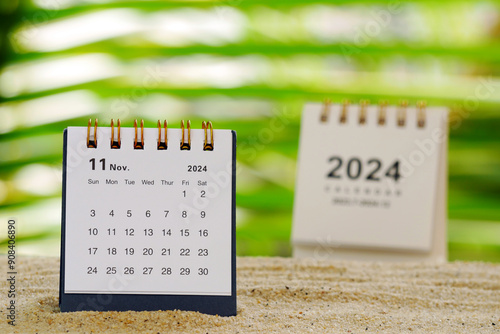 Two white desk calendars for November 2024 on a table with bokeh foliage background photo