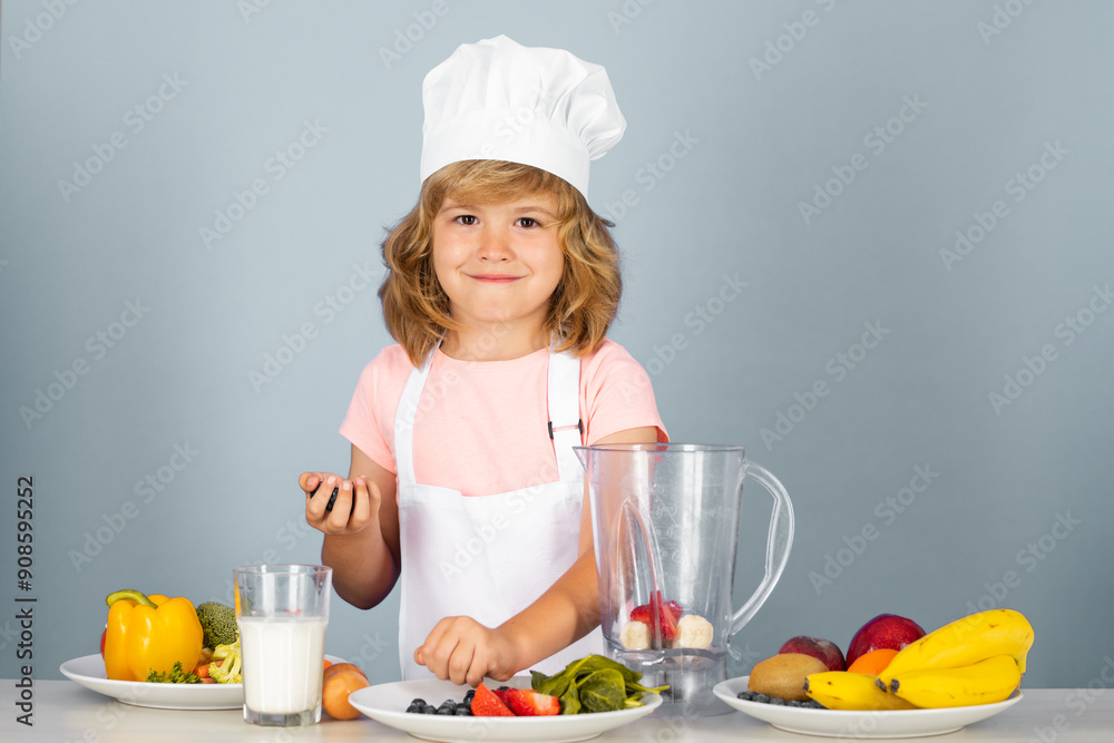 Child chef cook prepares food on isolated grey studio background. Kids cooking. Teen boy with apron and chef hat preparing a healthy vegetables meal in the kitchen. Child chef cook prepares food on isolated grey studio background. Kids cooking. Teen boy with apron and chef hat preparing a healthy vegetables meal in the kitchen.