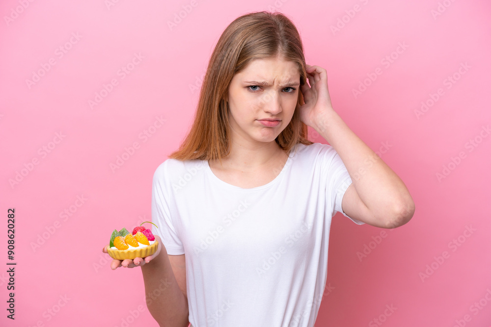 Teenager Russian girl holding a tartlet isolated on pink background having doubts Teenager Russian girl holding a tartlet isolated on pink background having doubts