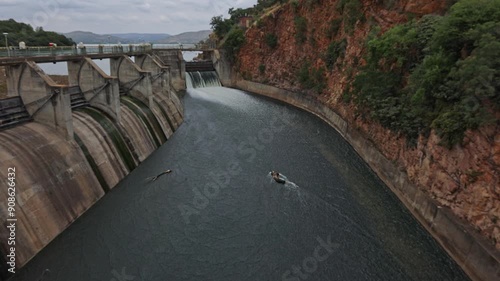 Water overflowing along a wide spillway between the wall of the dam and tall cliffs in order to maintain downstream water flow at Hartbeespoort dam close to Johannesburg and Pretoria in South Africa.