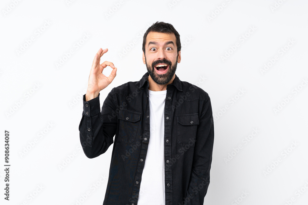 Young man with beard over isolated white background surprised and showing ok sign Young man with beard over isolated white background surprised and showing ok sign