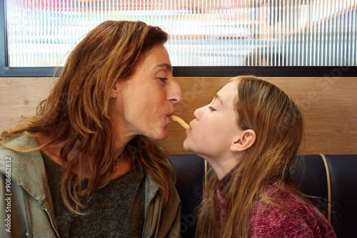 Daughter and mother playing together to eat a french fry in a restaurant