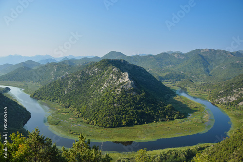 Observation deck Pavlova Strana in Montenegro. The mountain is surrounded by the horseshoe-shaped Crnojevica River. Mountain range covered with green forest, clear blue sky.