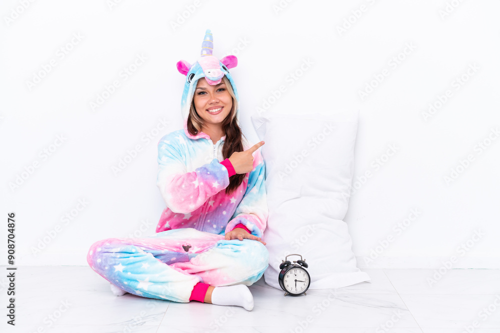 Young Russian girl wearing a unicorn pajama sitting on the floor isolated on white background pointing back Young Russian girl wearing a unicorn pajama sitting on the floor isolated on white background pointing back