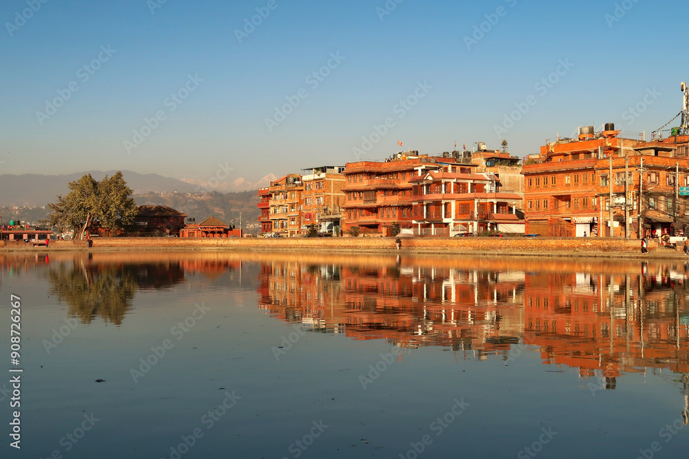 Obraz premium Golden hour at the Na Pukhu Lake, Pond in Bhaktapur, apartment, residential houses, buildings, dwellings are reflecting perfectly in the smooth surface of the water Bhaktapur, Nepal