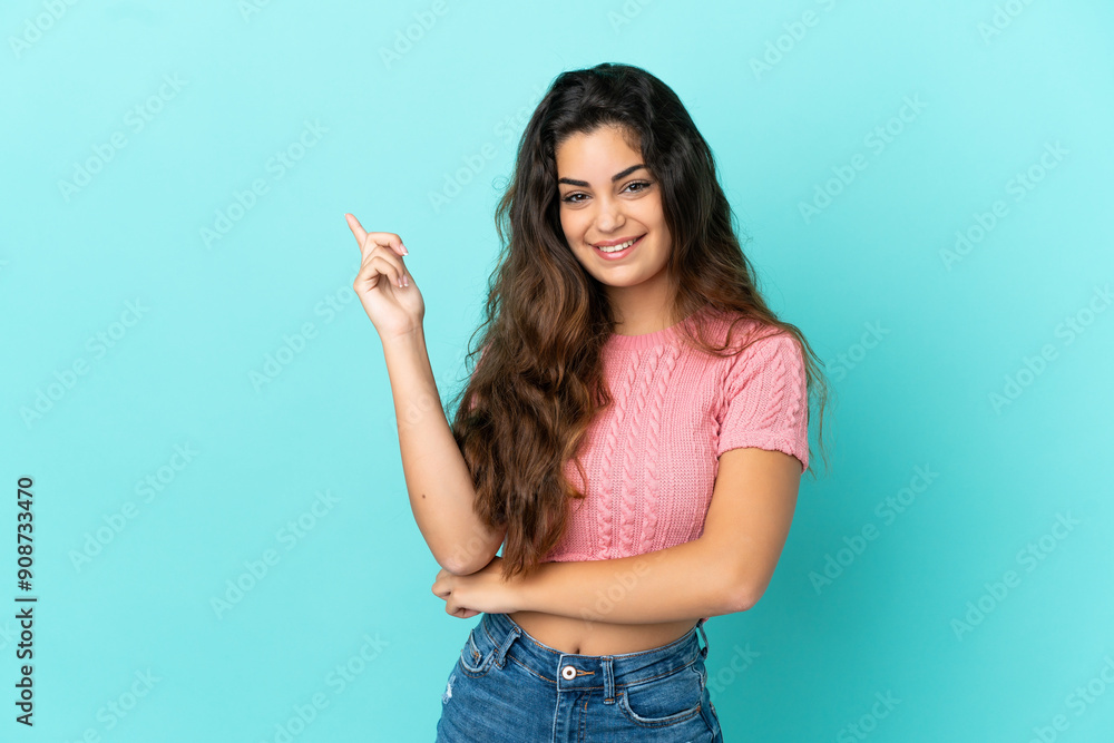 Young caucasian woman isolated on blue background happy and pointing up Young caucasian woman isolated on blue background happy and pointing up