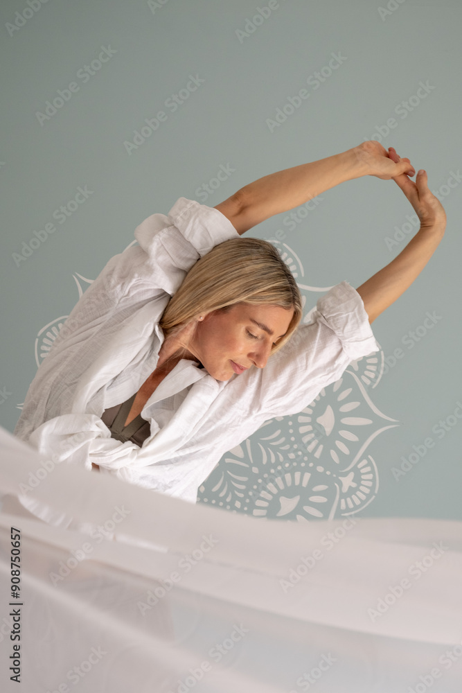 One woman in a yoga studio wearing a white shirt, stretching her arms ...
