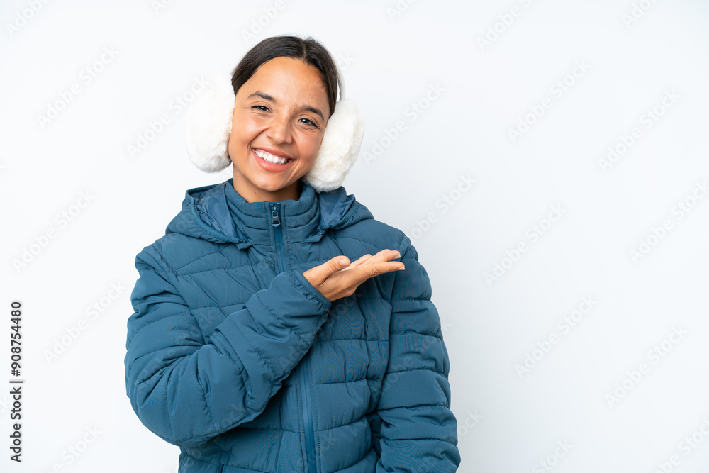 Young hispanic woman wearing a winter earmuffs isolated on white background presenting an idea while looking smiling towards Young hispanic woman wearing a winter earmuffs isolated on white background presenting an idea while looking smiling towards