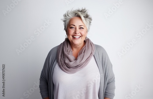 On a grey backdrop, a plump elderly blonde exudes confidence and charm, embracing her full-figured, matured grace