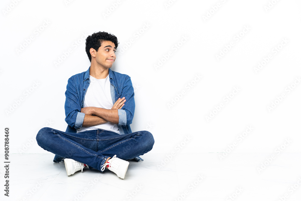 Venezuelan man sitting on the floor making doubts gesture while lifting the shoulders Venezuelan man sitting on the floor making doubts gesture while lifting the shoulders