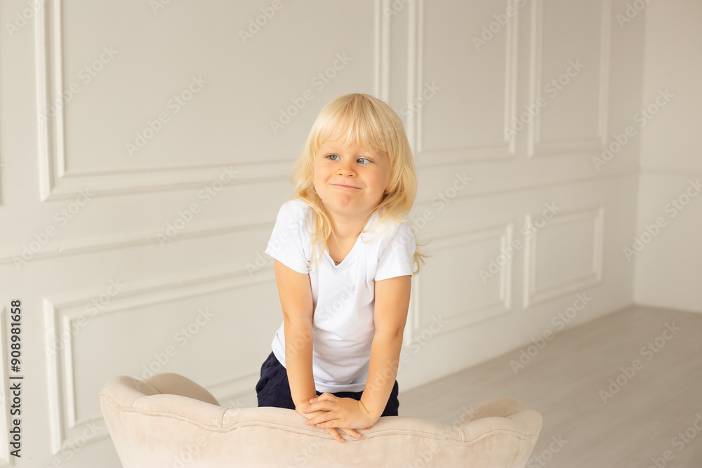 Little boy at home with strabismus eyes, squinting eyes. Child boy wearing white t-shirt on a beige chair