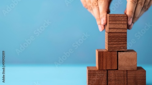 Hands carefully placing a wooden block on top of a growing tower, symbolizing building, growth, and success.