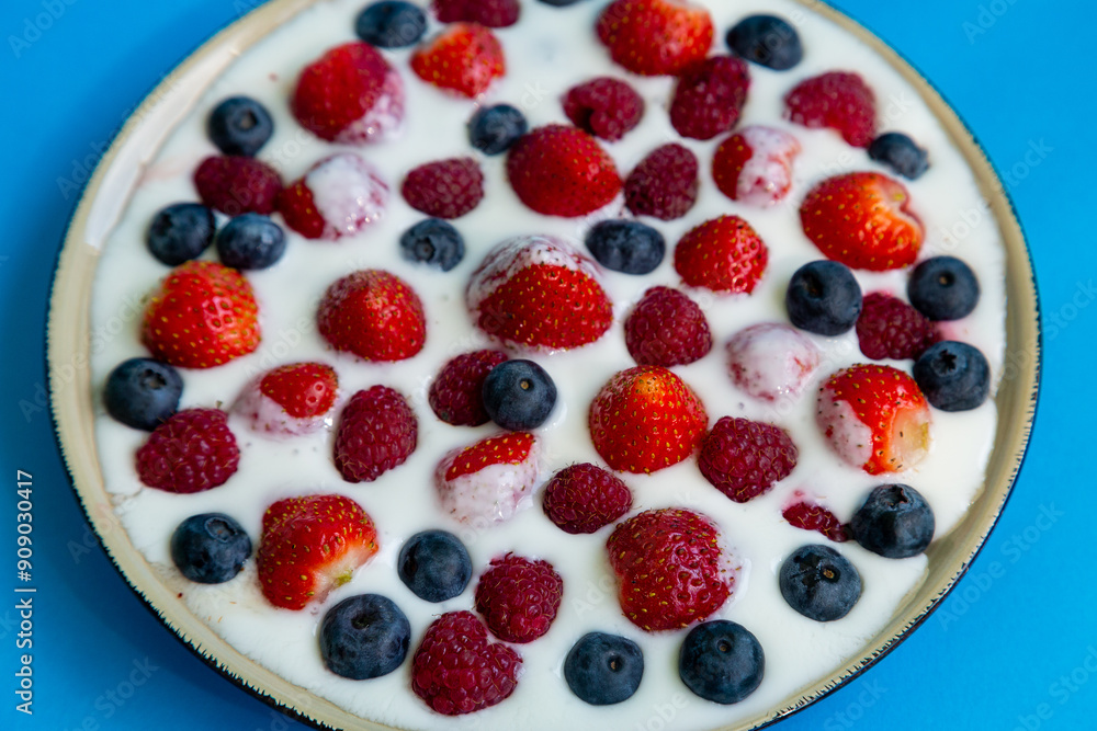 In a plate with whipped cream ripe berries strawberries raspberries and blueberries on a blue background In a plate with whipped cream ripe berries strawberries raspberries and blueberries on a blue background