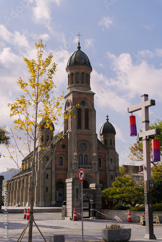 the Jeondong Catholic Church with its twin bell towers, a statue of Jesus, clear skies, and two people near a cleaning cart. photo