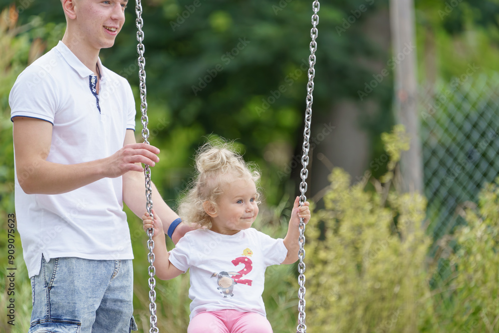A young father pushes his little daughter on a swing in the park.