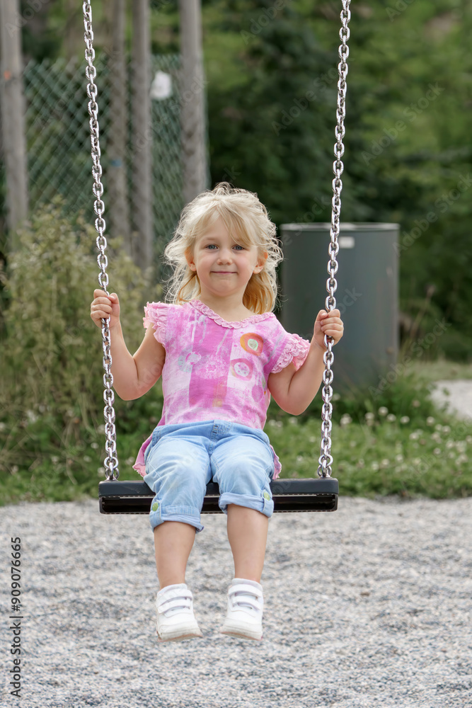 A little girl is riding on a chain swing in a park. A little girl is riding on a chain swing in a park.