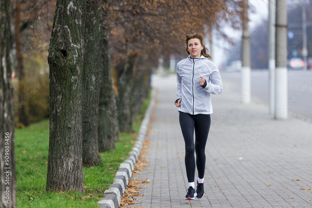Woman Running Along Tree-Lined Pathway in Early Morning Fog Woman Running Along Tree-Lined Pathway in Early Morning Fog